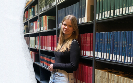 Julie leunt tegen een boekenkast in de bib